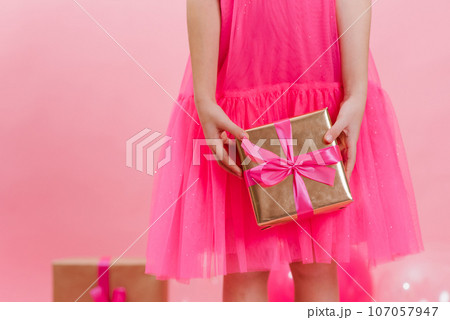 Girl is holding a golden gift with a pink fuchsia ribbon on a pink background. It's time to pack gifts. The concept of surprise is to surprise loved ones 107057947