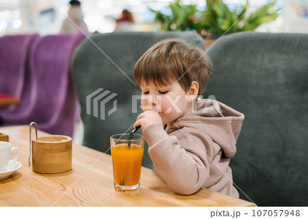 Little boy child drinks juice from a straw while sitting at a table in a cafe Little boy child drinks juice from a straw while sitting at a table in a cafe 107057948
