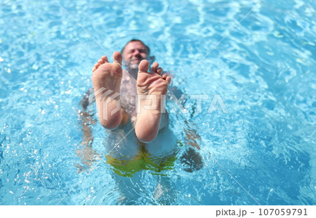 Man shows his feet while lying in pool Man shows his feet while lying in pool 107059791