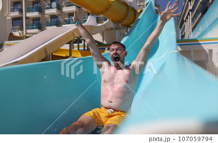 Joyful man slides down slide in water park 107059794