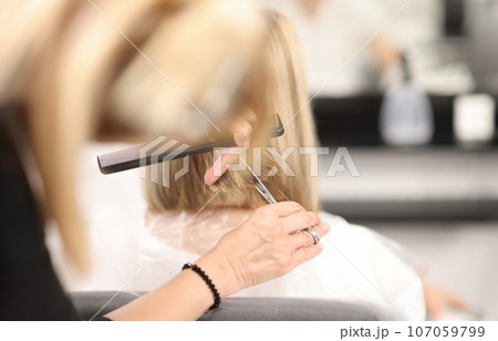 Hairdresser holds comb and scissors in his hands and cuts client's hair 107059799