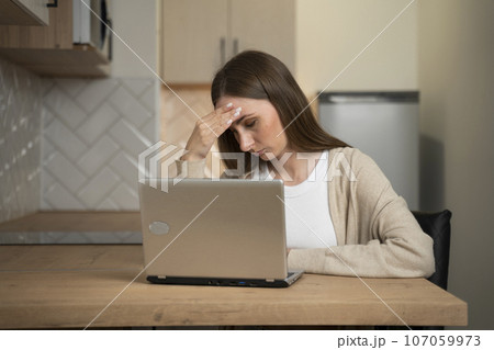 The concept of remote work, business and people is a tense or tired young woman with a laptop computer working in a home office in the kitchen 107059973