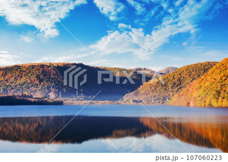 mountainous countryside landscape with lake in autumn. scenery in fall colors. bright sunny weather with clouds on the sky. cluj county, romania 107060223