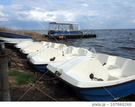 Spring landscape with catamaran and water bikes on the shore of a large lake, against a clear sky. Rural landscape, a beautiful place to relax. 107060260