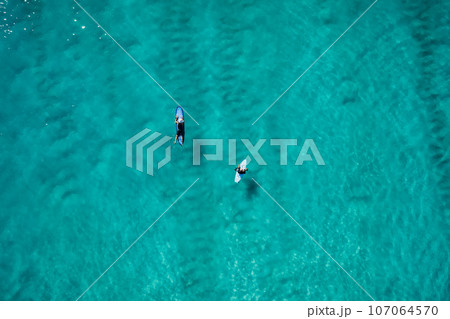 Surfers rowing on surfboards in transparent turquoise ocean waiting wave. Aerial view Surfers rowing on surfboards in transparent turquoise ocean waiting wave. Aerial view 107064570