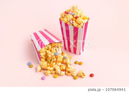 Two striped carton buckets with caramel popcorn and dragee candies on pink background Two striped carton buckets with caramel popcorn and dragee candies on pink background 107064941