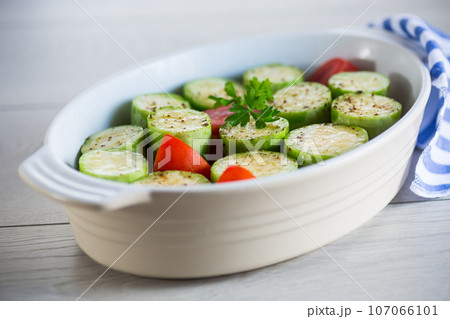 Raw zucchini with tomatoes prepared for baking in a ceramic form. 107066101