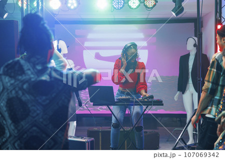 Woman musician using dj controller while performing on stage in nightclub. African american disc jokey playing and mixing electronic music during concert disco party in club 107069342