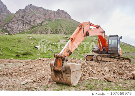 Excavator works in the highlands. Clears the consequences of a mudslide in the gorge of the mountains. repair and expansion of a road Excavator works in the highlands. Clears the consequences of a mudslide in the gorge of the mountains. repair and expansion of a road 107069979