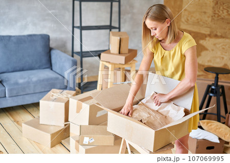 Young girl packing plates into the boxes ready to move. Woman unpacking moving boxes in her new home. unpack personal stuff from carton boxes. 107069995