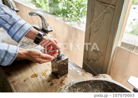 A man's hand touches the water in a beautiful sink with a metal faucet next to an mirror. Close-up of an elegant faucet in the bathroom sink next to stylish decorations. A man's hand touches the water in a beautiful sink with a metal faucet next to an mirror. Close-up of an elegant faucet in the bathroom sink next to stylish decorations. 107070003