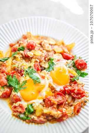 Shakshouka for breakfast. Homemade shakshuka, fried eggs, onion, bell pepper, tomatoes and parsley in a pan. Marble background. Top view. chakchouka Shakshouka for breakfast. Homemade shakshuka, fried eggs, onion, bell pepper, tomatoes and parsley in a pan. Marble background. Top view. chakchouka 107070007