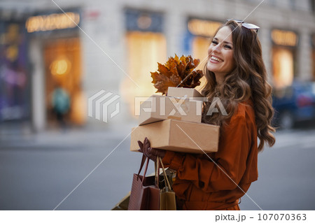 smiling young woman in orange trench coat with parcels smiling young woman in orange trench coat with parcels 107070363