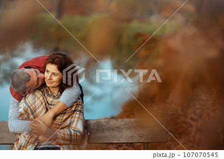 smiling romantic couple in park kissing while sitting on bench 107070545