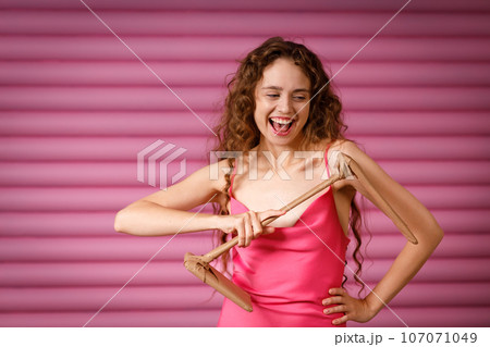 Young positive smiling woman receives a gift and holds in her hands a table electric lamp wrapped in rustic beige craft paper on pink background. Black Friday concept. 107071049