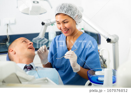 Positive female dentist preparing for male oral examination 107076852