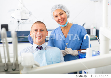 Dentist and happy patient sitting in dental chair 107076877