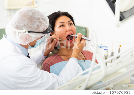 Dentist filling teeth for woman patient sitting in medical chair Dentist filling teeth for woman patient sitting in medical chair 107076953