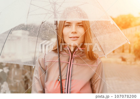 Woman rain umbrella. Happy woman portrait wearing a raincoat with transparent umbrella outdoors on rainy day in park near sea. Girl on the nature on rainy overcast day. Woman rain umbrella. Happy woman portrait wearing a raincoat with transparent umbrella outdoors on rainy day in park near sea. Girl on the nature on rainy overcast day. 107078200