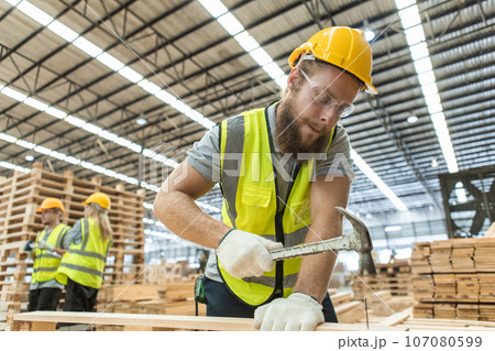 Male engineer carpenter wearing safety uniform and yellow hard hat working using hammer nail 107080599