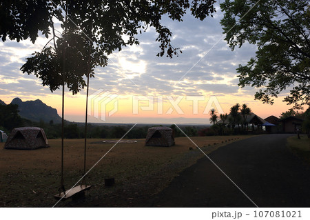 A photo taken in the morning before sunrise inside Phu Pha Man National Park, Thailand. Tourist tents are visible in a wide field inside the park. In the foreground, there is a swing tied to a tree. A photo taken in the morning before sunrise inside Phu Pha Man National Park, Thailand. Tourist tents are visible in a wide field inside the park. In the foreground, there is a swing tied to a tree. 107081021