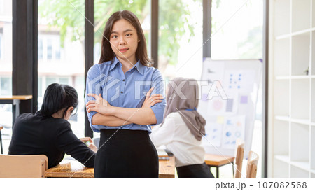 A confident Asian businesswoman is standing in the meeting with her arms crossed. A confident Asian businesswoman is standing in the meeting with her arms crossed. 107082568