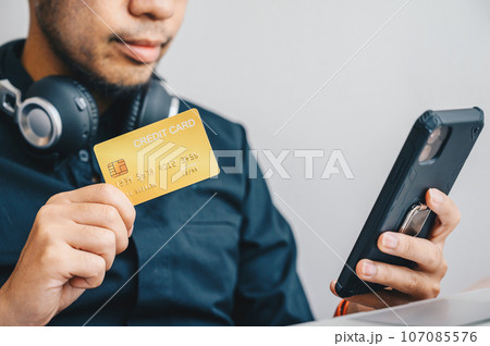 Close-up of businessman holding gold credit card for payment online shopping on smartphone. Credit card lets cardholders borrow funds with which to pay for goods and services depend on the condition. 107085576