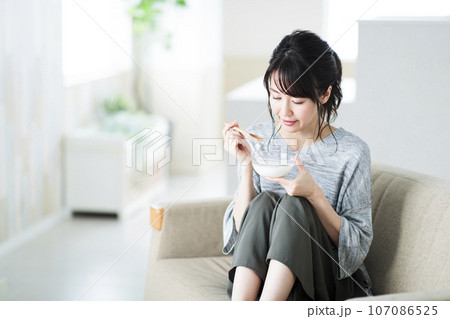 リビングでヨーグルトを食べる若い女性 リビングでヨーグルトを食べる若い女性 107086525