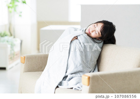 リビングのソファでブランケットを羽織る若い女性 107086556