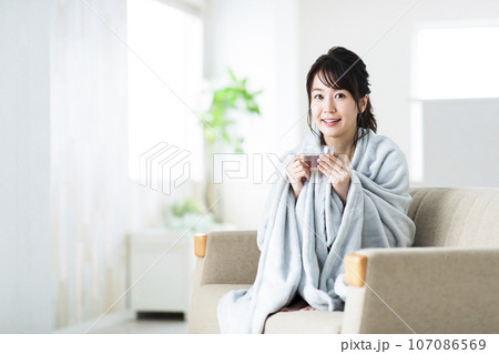 リビングのソファでブランケットを羽織る若い女性 107086569