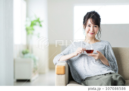 リビングのソファに座って紅茶を飲む若い女性 107086586