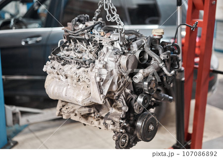 A car mechanic inspects the engine with a flashlight. Engine Block on a repair stand with Special crane jack. Technical service station for car. A car mechanic inspects the engine with a flashlight. Engine Block on a repair stand with Special crane jack. Technical service station for car. 107086892