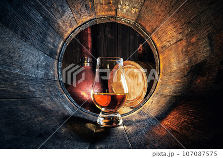 A glass of whiskey in oak barrel 107087575