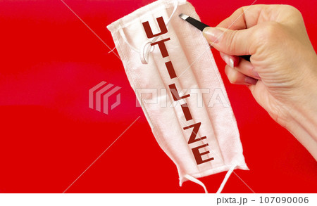 A woman's hand holds a medical mask with the text Utilize, on a red background. Infection atmosphere 107090006