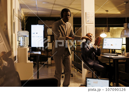 Cheerful happy worker having fun in startup office, listening music while showing funny dance moves. Executive manager working overtime at company investment plan. Business concept Cheerful happy worker having fun in startup office, listening music while showing funny dance moves. Executive manager working overtime at company investment plan. Business concept 107090126