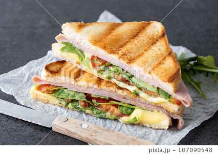 Panini sandwich with ham, cheese, tomato and arugula on black slate background 107090548