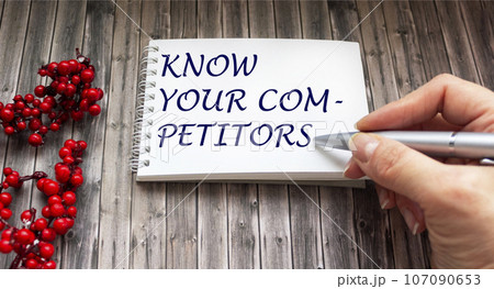 KNOW YOUR COMPETITOR. Wooden table with writing message by female hand 107090653