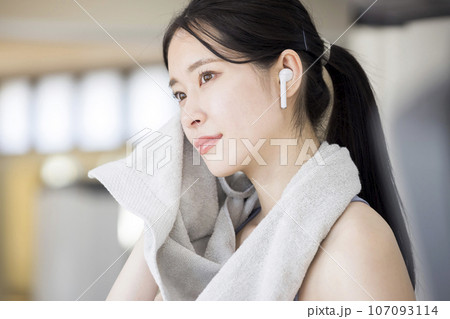 スポーツジムで汗を拭くワイヤレスイヤホンをした若い女性 107093114