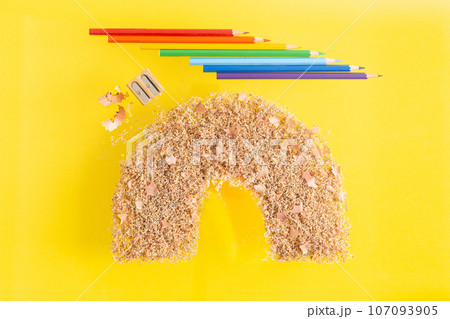 Coloured pencils and pencil shaving and sawdust on yellow background in form of rainbow. School Coloured pencils and pencil shaving and sawdust on yellow background in form of rainbow. School 107093905