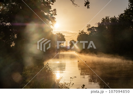 Mystical Sunset Mist Over Canal: Golden Rays Illuminating Tranquility Mystical Sunset Mist Over Canal: Golden Rays Illuminating Tranquility 107094850