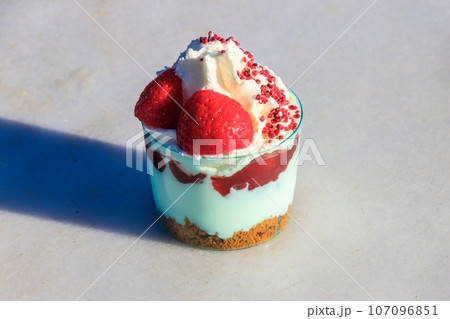 Strawberry trifle with whipped cream, berry sauce and cookie crumbs in a glass on a gray concrete background 107096851