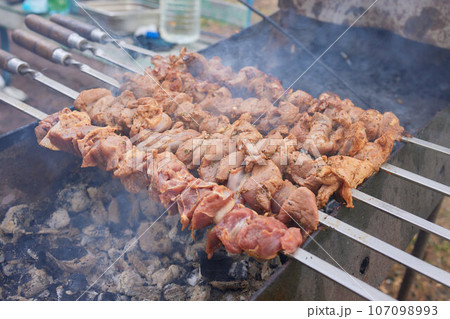 Closeup of marinated big turkey or chicken meat steak shashlik or shish kebab preparing cooking on barbecue brazier grill over charcoal on burning coal. Skewered roasted kebabs on BBQ grill 107098993