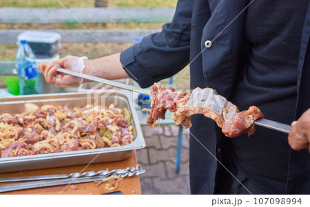 Closeup of marinated big turkey or chicken meat steak shashlik or shish kebab preparing cooking on barbecue brazier grill over charcoal on burning coal. Skewered roasted kebabs on BBQ grill 107098994