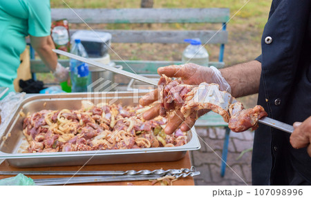 Closeup of marinated big turkey or chicken meat steak shashlik or shish kebab preparing cooking on barbecue brazier grill over charcoal on burning coal. Skewered roasted kebabs on BBQ grill 107098996