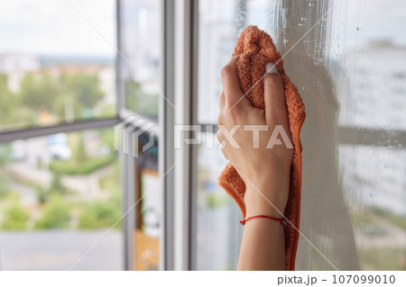 Young woman cleaning window glass with rag at home, closeup. Young woman cleaning window glass with rag at home, closeup. 107099010