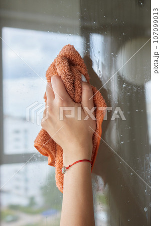 Young woman cleaning window glass with rag at home, closeup. Young woman cleaning window glass with rag at home, closeup. 107099013