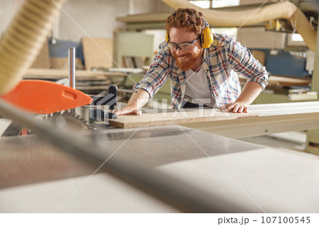Male carpenter sawing a board with a circular saw in a carpentry workshop. High quality photo 107100545