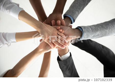 Close up of diverse colleagues join hands showing unity Close up of diverse colleagues join hands showing unity 107102339