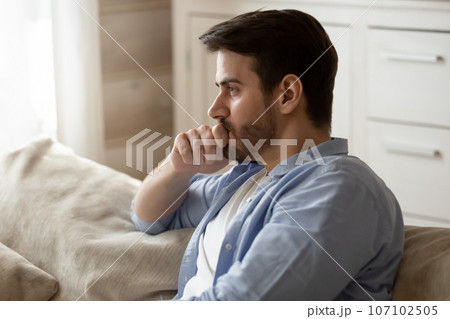 Thoughtful upset man pondering problem solving, sitting on couch 107102505