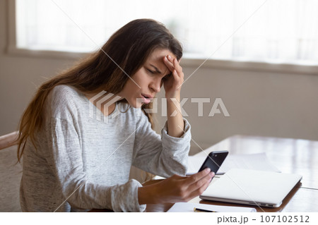 Angry young woman looking at phone screen, reading bad news 107102512